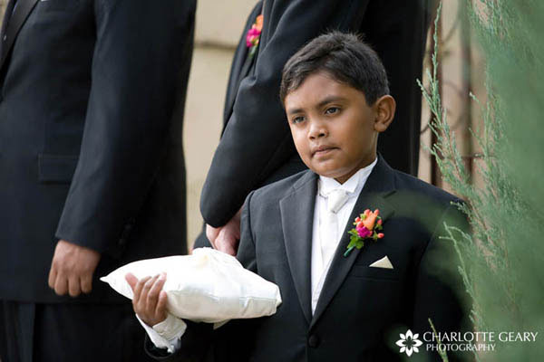 Ring bearer in black suit, white tie, and orange and pink boutonniere